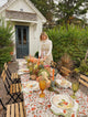 Female setting a fall table with block printed tablecloth, flowers, gourds and plates