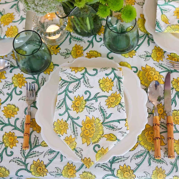 Table setting on yellow and green block printed tablecloth with plate, napkin, bamboo silverware and flowers