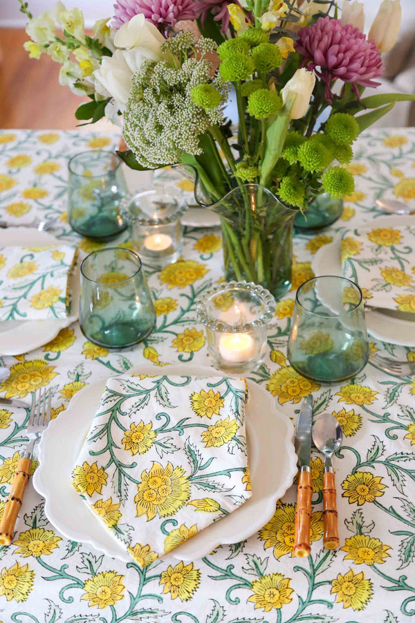 Plate and napkin on yellow and green block printed tablecloth with bamboo silverware and flowers