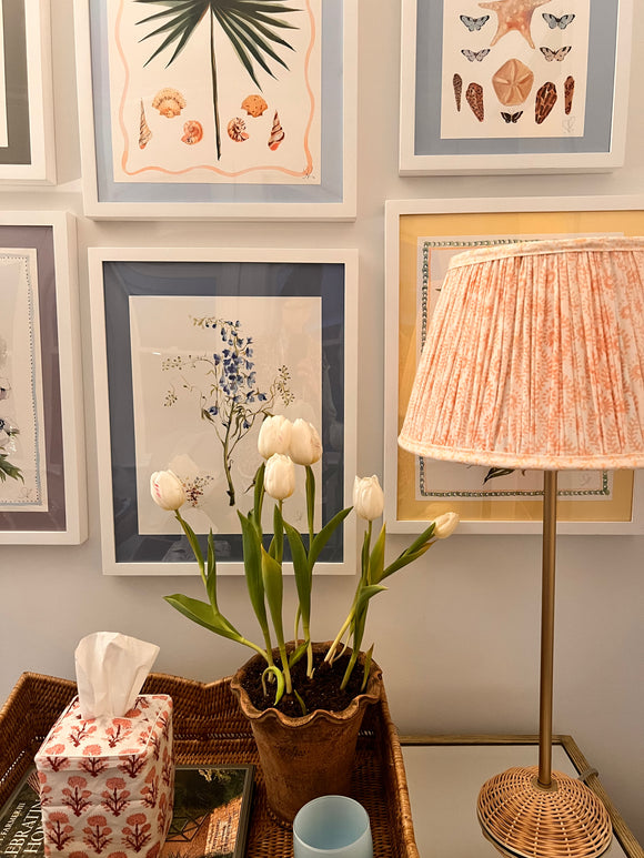 Pink block printed lampshade on table beside flowers and paintings