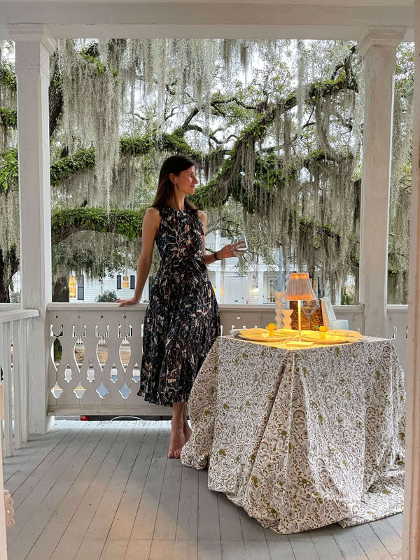 Girl standing on front porch beside square table with tablecloth and cordless lamp