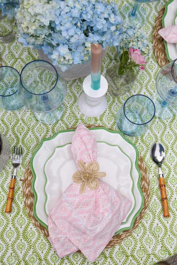 Table setting with pink napkin on plate with blue flowers on a green block printed tablecloth